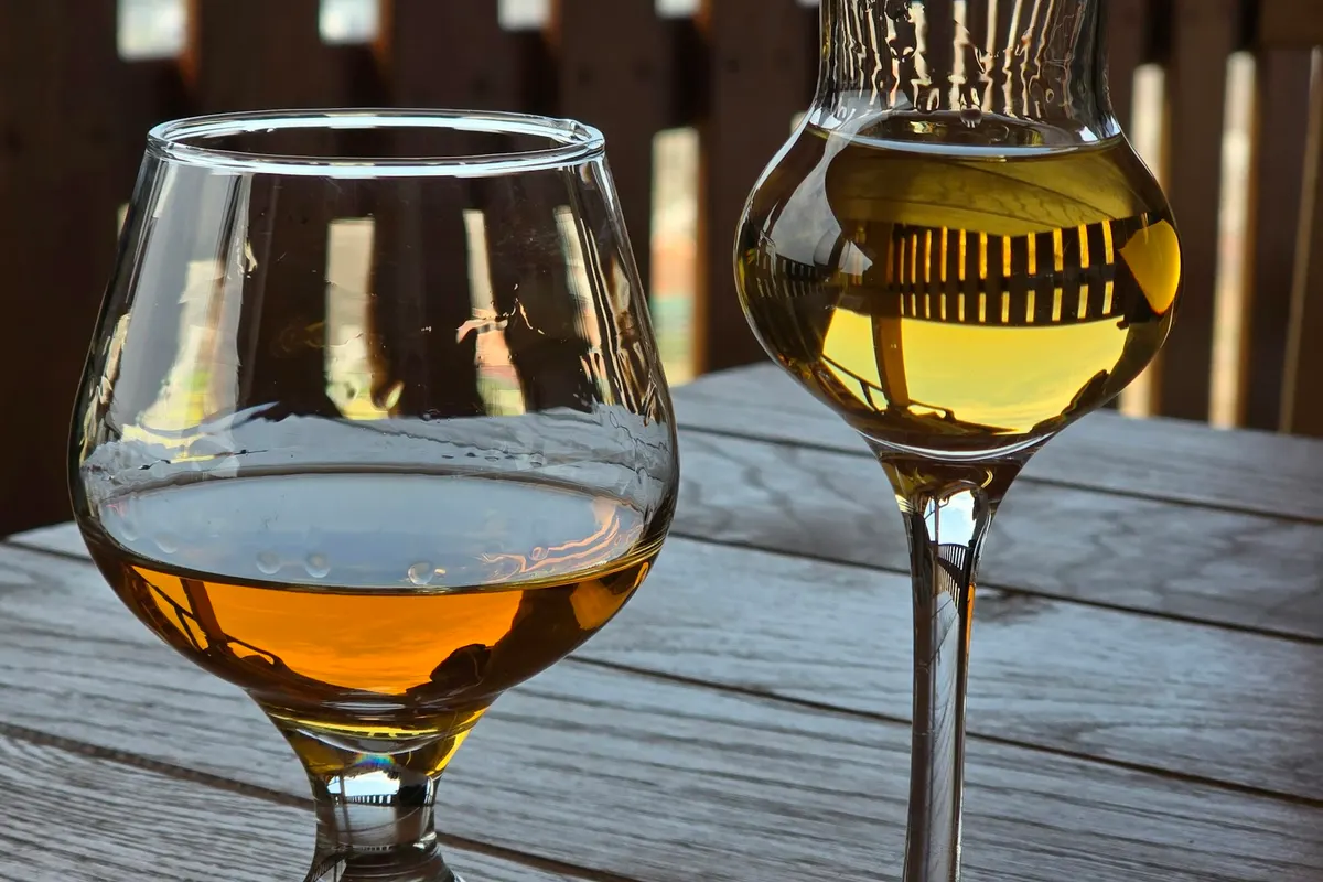 A brandy snifter and a tulip glass of amber spirit on a wooden table