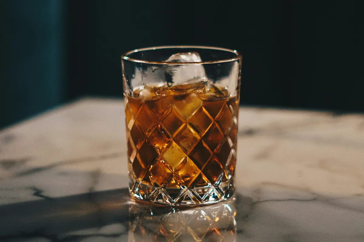 A cut-crystal glass of bourbon over ice on a marble surface
